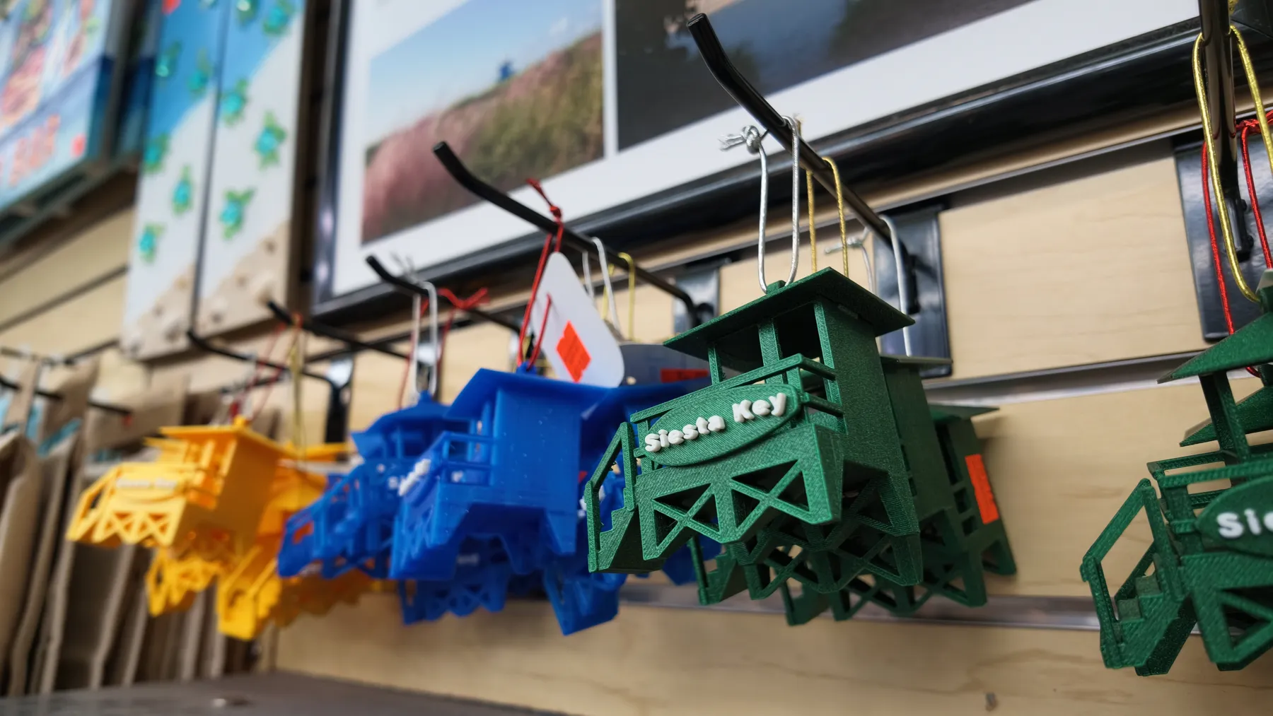 Yellow, blue and green miniature Siesta Key lifeguard shacks hanging on hooks in a gift shop